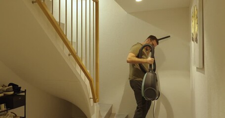 A man cleans high corners and stairs using an old wired vacuum cleaner. Outdated cleaning concept, housework, and daily chores.