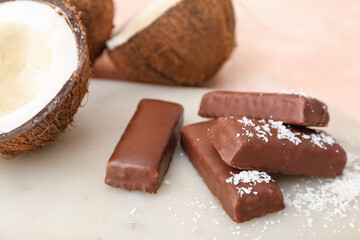 Board with tasty chocolate covered coconut candies on beige background