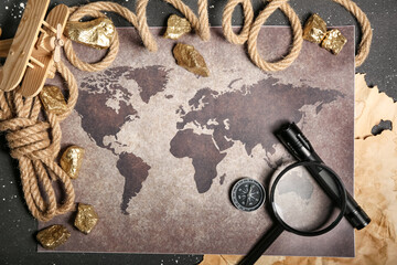 World map with travel equipment, airplane toy and golden nuggets on grunge black background