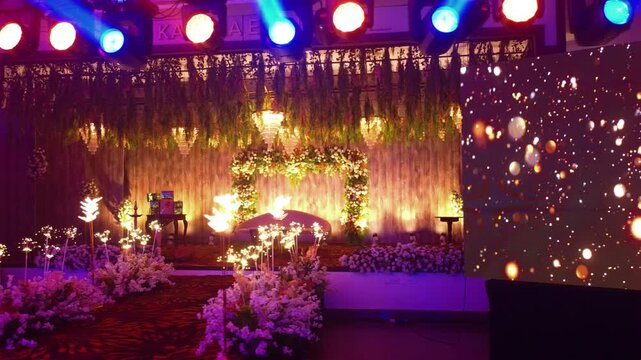 Luxurious wedding or reception stage with floral arch, sofa, dramatic lighting, and large LED screen displaying golden bokeh motion graphics for an elegant event.