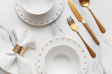 Elegant table setting with golden cutlery and folded napkin on white marble background