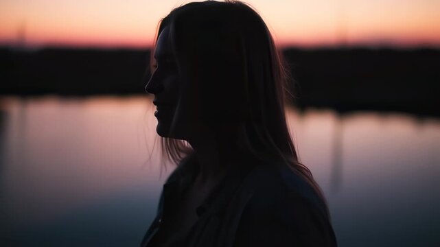 Silhouette of a woman's profile against a serene sunset sky, soft light reflects on water