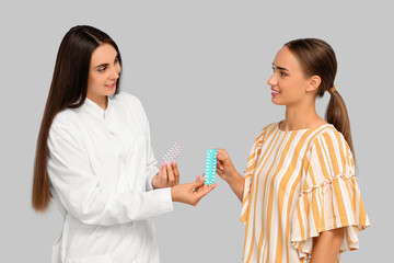 Female gynecologist with contraceptive pills and patient on light background