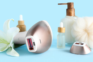 Modern photoepilator with cosmetic products, bath supplies and lily flower on blue background