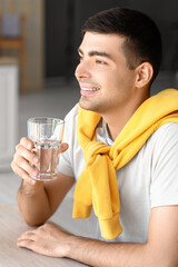 Young man with glass of fresh water sitting at table in kitchen