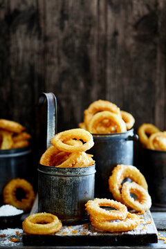 Crispy golden onion rings served in rustic metal cups on wooden surface