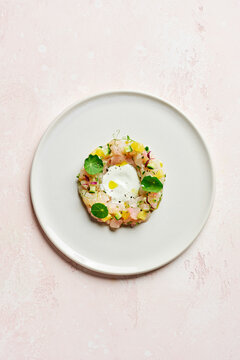 Overhead shot of snapper crudo (raw fish) with coconut, finger lime, cucumber, yuzu, yellow chilli oil and nasturtium leaves, on a pink surface with copy space