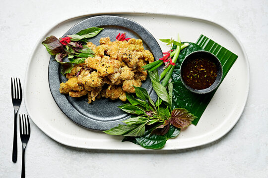 Sharing plate of crispy turmeric chicken with coriander dipping sauce on a platter with banana leaf, betel leaves, shiso leaves, Vietnamese mint, spring onions & pineapple sage flowers