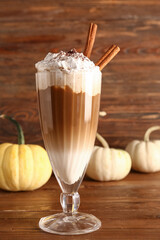 Glass of tasty pumpkin latte with cinnamon on wooden background