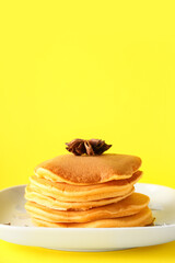 Plate with tasty pumpkin pancakes and star anise on yellow background