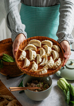 woman shef holding a bamboo tray with uncooked gyoza dumplings, bamboo steamer. teal teapot, fresh green onions, and mushrooms, Asian cuisine