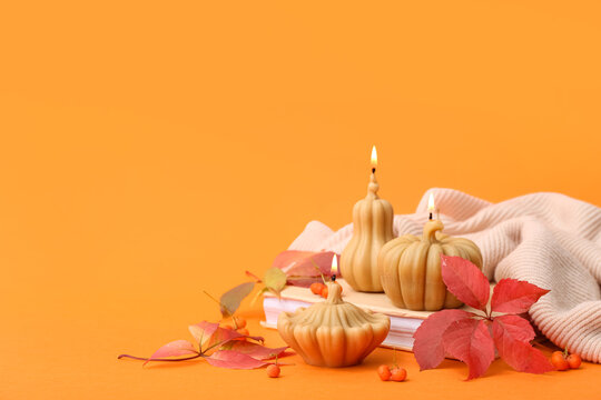 Beautiful composition with burning candles in shape of pumpkin, book and autumn leaves on orange background - Powered by Adobe