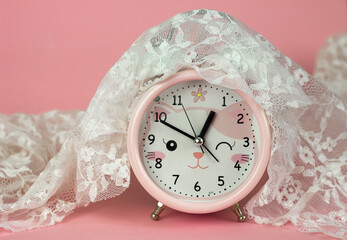 Pink alarm clock covered with lace on a pink background, seasonal change of clocks
