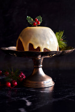 English style festive Christmas plum pudding dessert, served with traditional brandy custard, against black marble background.