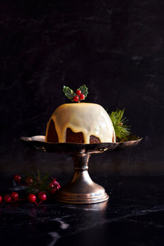 English style festive Christmas plum pudding dessert, served with traditional brandy custard, against black marble background.