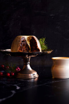 English style festive Christmas plum pudding dessert, served with traditional brandy custard, against black marble background.