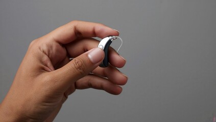 Hand holding a modern hearing aid with slim design and gray background  