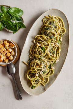 Plate of spaghetti with pesto. The surface is enhanced with a generous sprinkling of Parmigiano Reggiano, golden crouton crumbs, and fresh basil leaves.