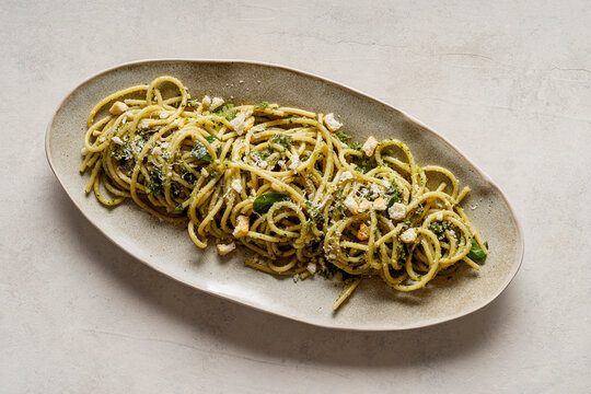 Plate of spaghetti with pesto. The surface is enhanced with a generous sprinkling of Parmigiano Reggiano, golden crouton crumbs, and fresh basil leaves.
