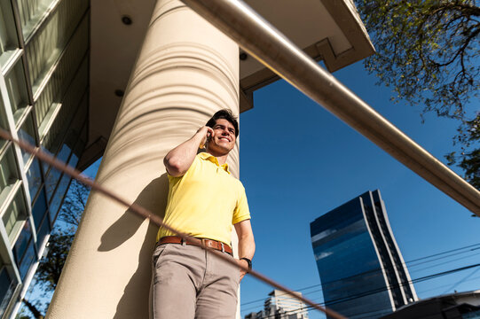 Urban entrepreneur talking on phone near modern column architecture