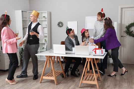 Happy young colleagues with champagne celebrating New Year at corporate party in office