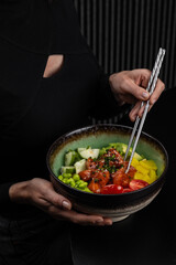 A girl uses chopsticks to take a piece of food from a poke bowl
