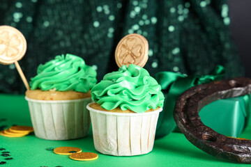 Tasty cupcakes with gift box, horseshoe and decor for St. Patrick's Day on color background