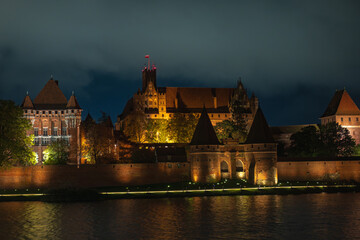 Obraz premium Nighttime Malbork Castle illuminated along the Nogat River, Poland