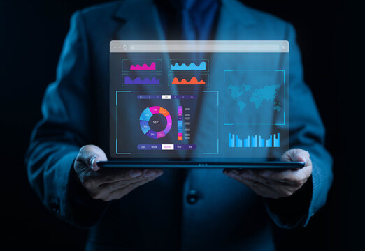 Businessman holding tablet with futuristic digital dashboard displaying data analytics, charts, and world map visualization. Concept of business intelligence, big data, and technology innovation.