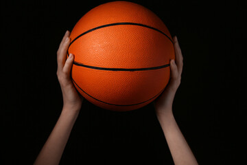 Young woman with ball for playing basketball on black background