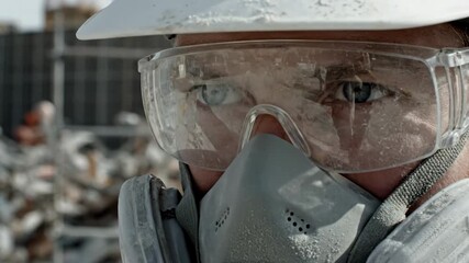 Construction employee protecting eyes and respiratory system with safety goggles, n95 respirator mask and hard hat while working in a dusty industrial area