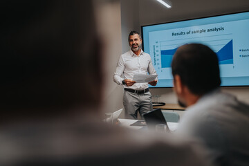 A confident presenter shares analysis results with colleagues in a modern boardroom, using a large screen chart to illustrate data trends during a professional business meeting.