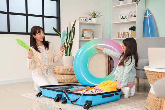 Young Asian mother and her daughter packing their suitcase at home. Travel concept - Powered by Adobe