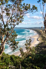 Scenic coastal view of waves and sandy beach framed by native Australian vegetation under a bright blue sky &ndash; nature landscape at Byron Bay, New South Wales, Australia