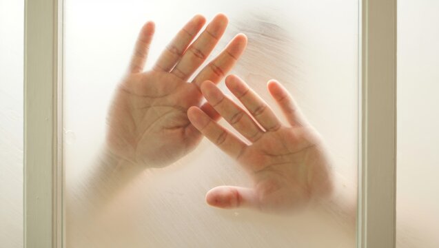 Hands pressing against privacy glass, creating a blurred silhouette, expressing feelings of fear, isolation, loneliness, and confinement in a stressful situation