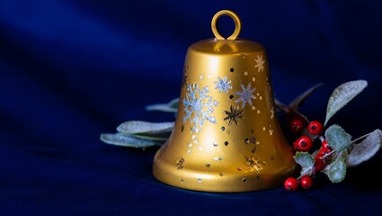 Golden bell ornament with sparkly snowflake patterns beside red berries and frosted leaves, glowing against deep blue background for festive holiday cards and designs