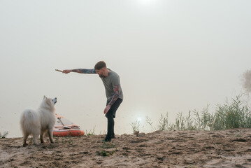 man playing with his cute samoyed dog at the lake during sunset