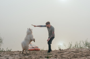 man playing with his cute samoyed dog at the lake during sunset