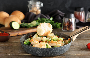 Frying pan with tasty chicken fillet, vegetables and bun on wooden table
