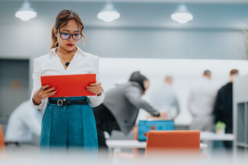 A confident Filipino woman wearing a white blouse and blue pants stands in a bright, modern office,...
