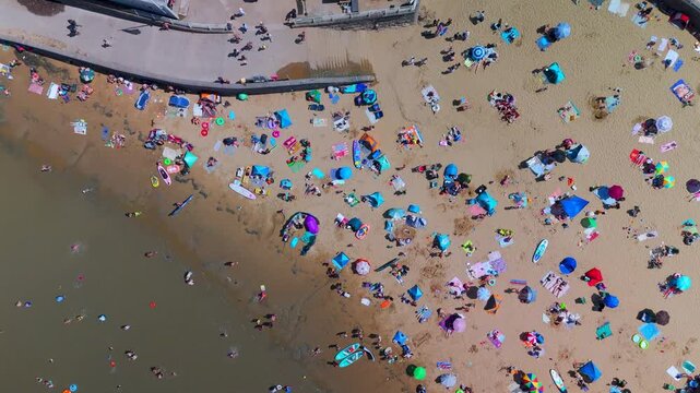 High angle aerial view of colorful parasols and sunbathers enjoying the summer sun on Marine Lake Beach, Weston-super-Mare, England.