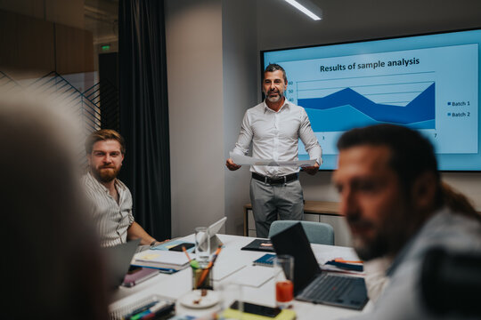 A professional presenter leads a meeting in a modern office, showing a data chart on a screen while colleagues discuss results, highlighting collaboration and data-driven decision making.