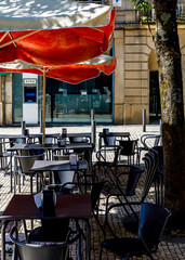 An empty outdoor cafe with tables and chairs under a red and white umbrella.