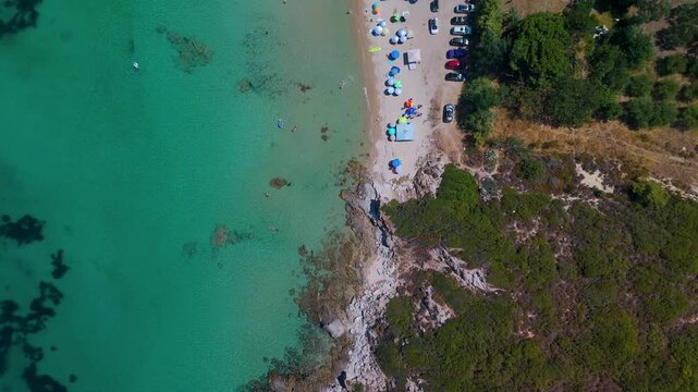 Vertical top-down aerial drone view of the rugged, rocky coastline and sandy beach of Nea Peramos in the Kavala region of Eastern Macedonia, Greece.