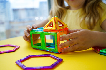 The photograph captures a little girl playing with magnetic construction blocks, assembling them...