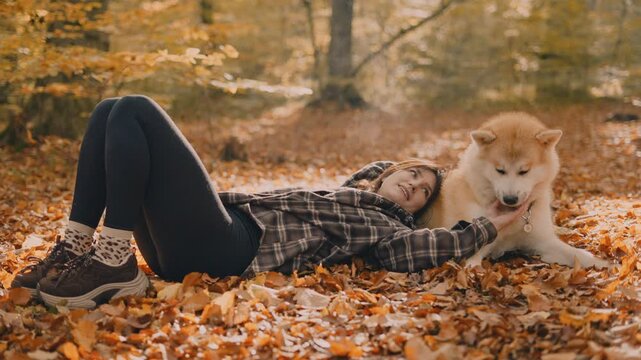 young woman walking and playing with her japanese akita puppy in autumn forest