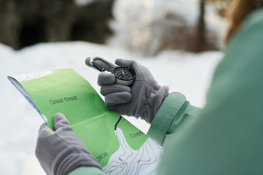 Caucasian young adult woman holding map and compass navigating snowy forest terrain, wearing gloves and outdoor jacket, focusing on route planning during winter adventure