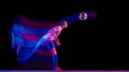 Female football player heading ball under glowing studio light. Concept of reaction training, coordination visuals, team sport branding, and modern athletic advertising.