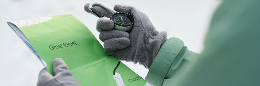 Caucasian young adult holding compass and map with gloved hands, navigating outdoors in winter setting, focusing on direction and location, exploring Great forest area - Powered by Adobe