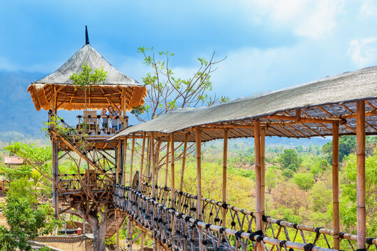 Happy family in bamboo treehouse with rooftop lookout and hanging bridge in Tulamben, Bali. Surrounded by lush tropical greenery and mountains, perfect for eco-tourism and adventure travel photography